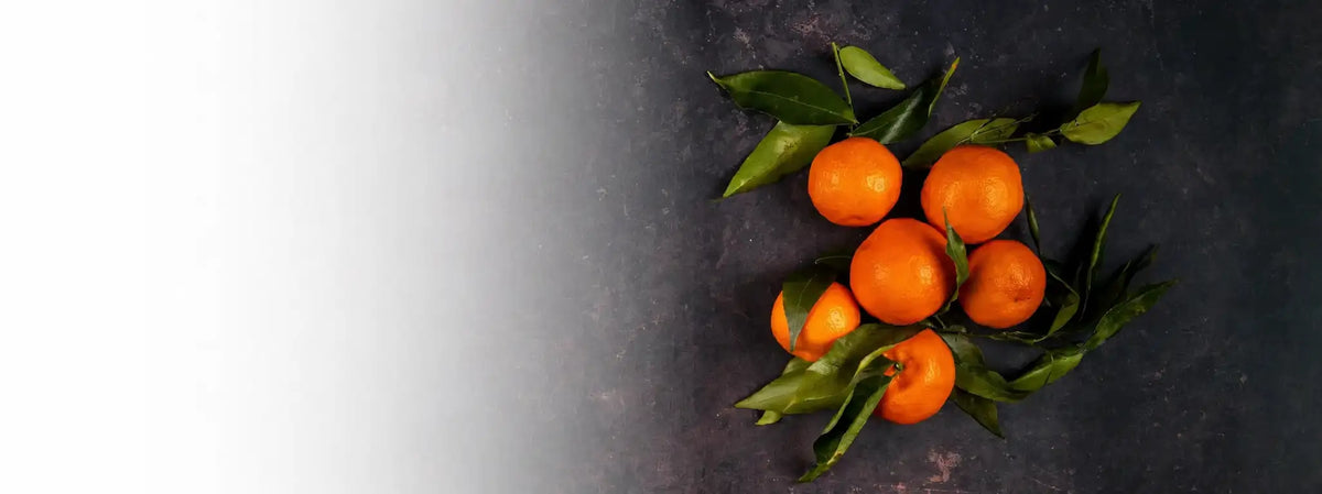 Ein Cluster aus leuchtend orangefarbenen Mandarinen mit frischen grünen Blättern, die noch daran befestigt sind.