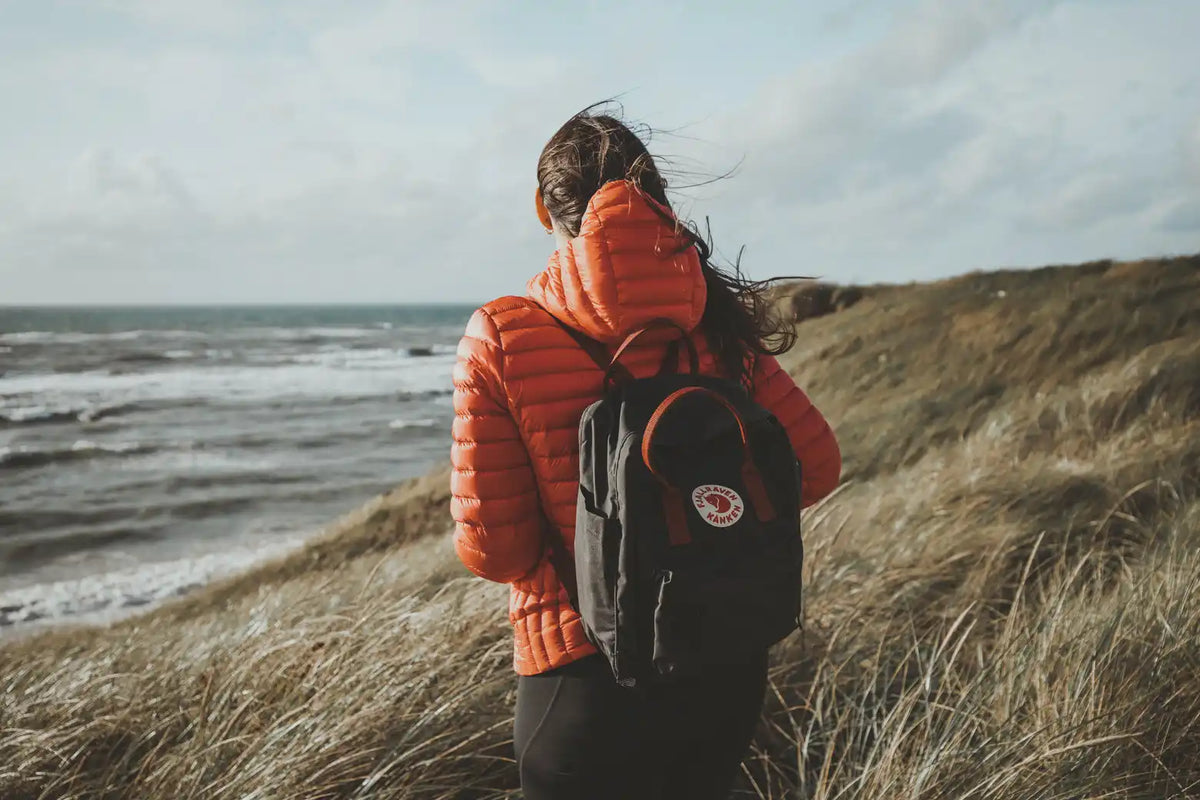 Schwarzer Fjällräven-Rucksack mit rundem Logo und orangefarbener Steppjacke